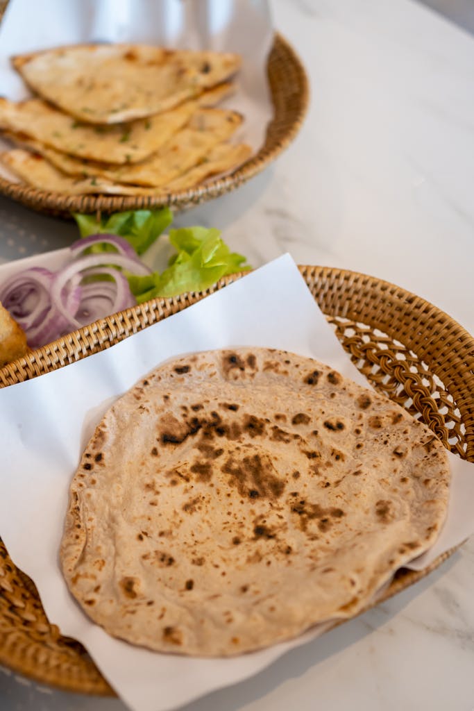 Close-up of freshly cooked Indian flatbread served in a wicker basket on a white table.
