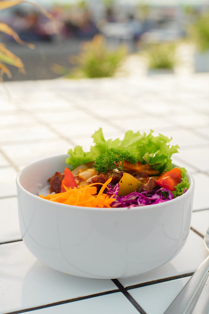 Colorful fresh salad bowl filled with vegetables on a sunlit tile table.